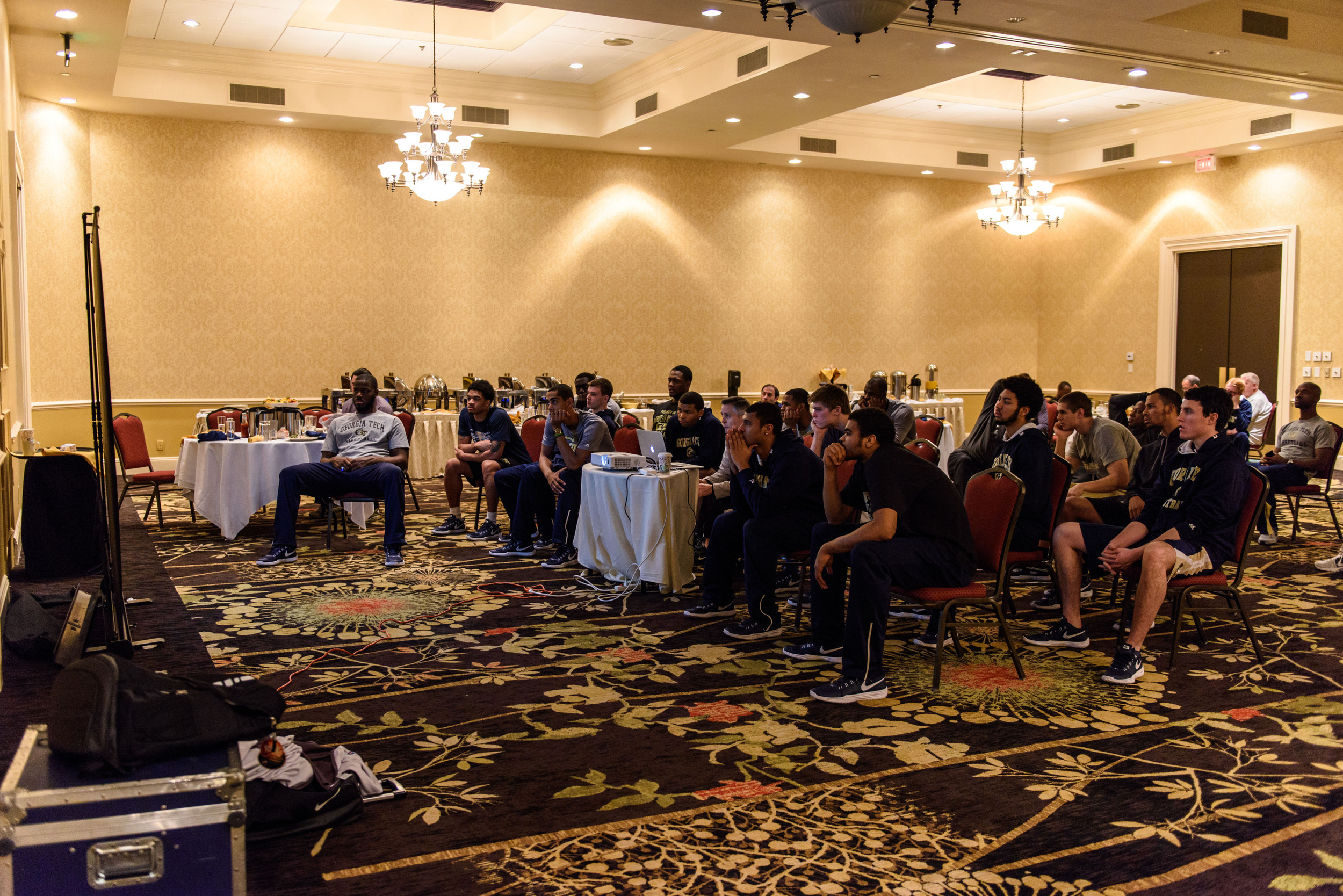 The team is focused on the screen as Coach Gregory points out things on the film.