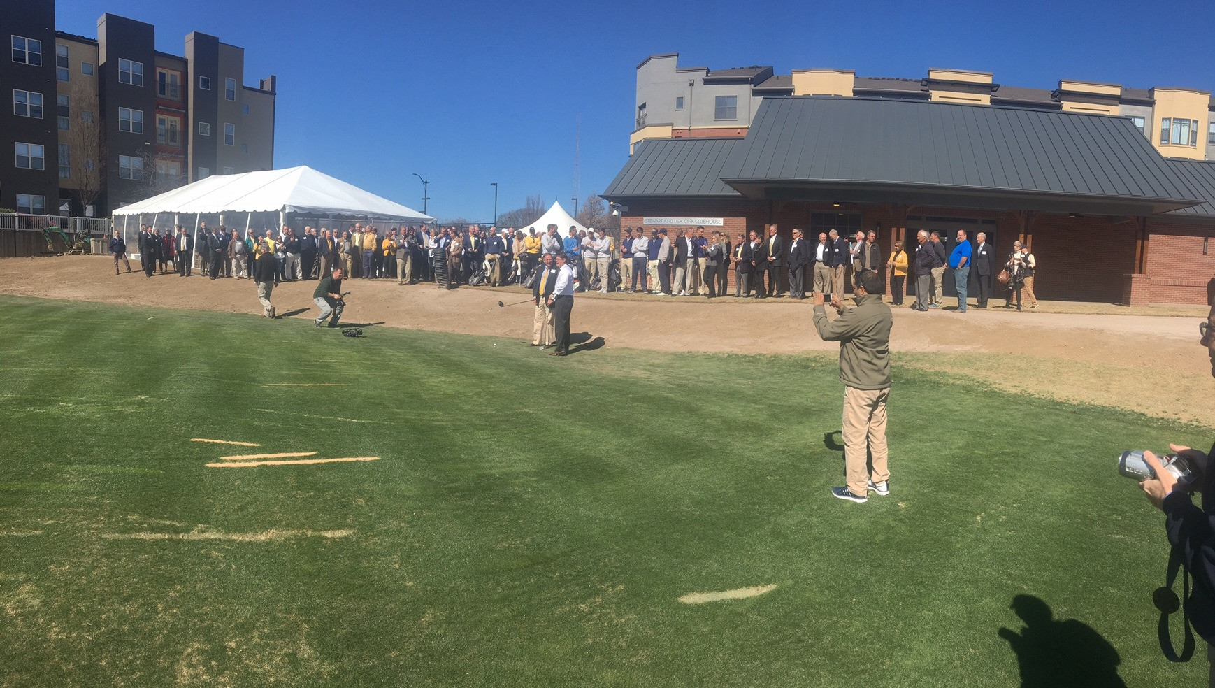 Panoramic shot of the attendees watching Tom Noonan prepare to hit the ceremonial first shot